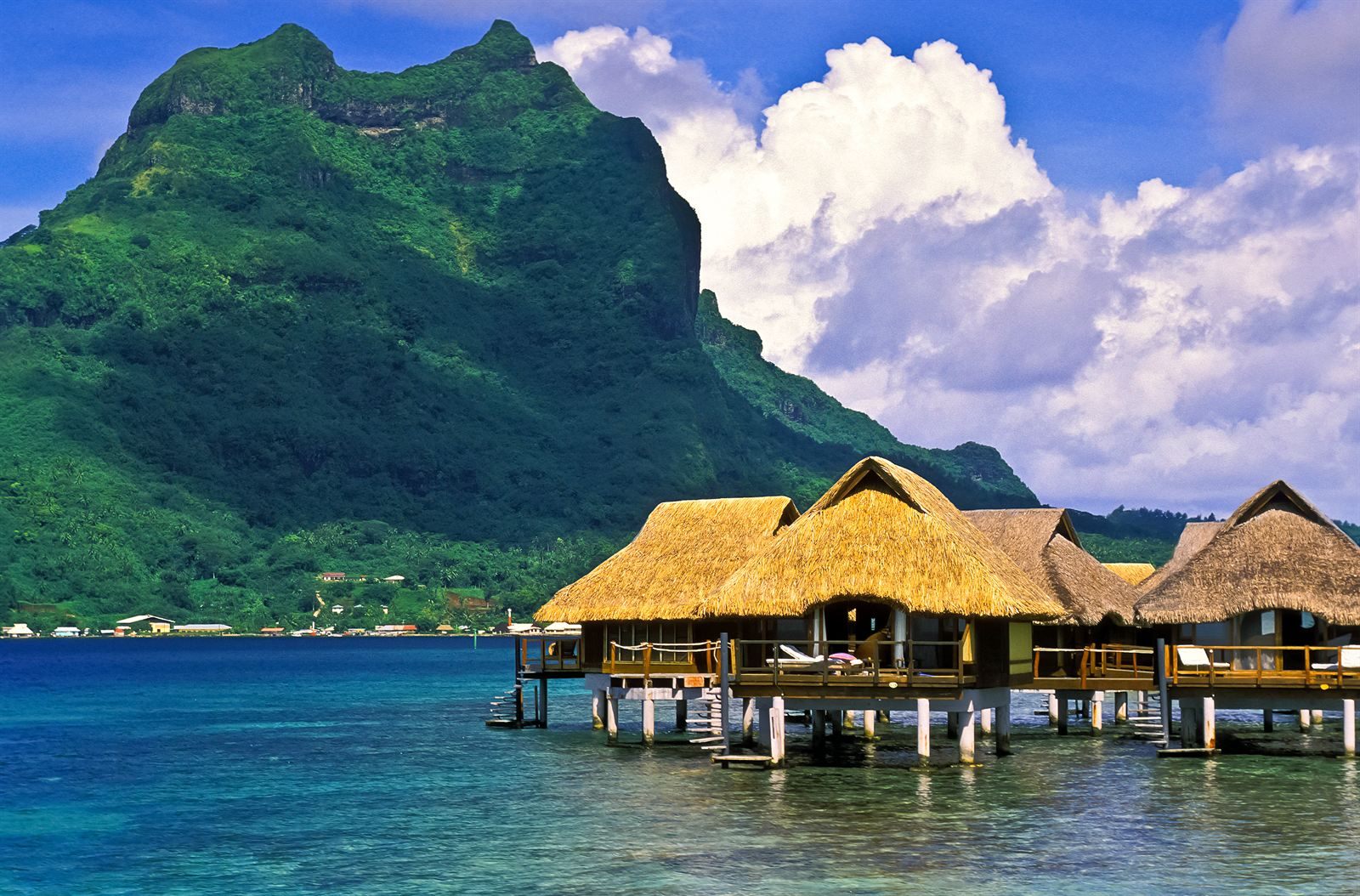 Overwater bungalows in a turquoise lagoon below a green peak, Fiji